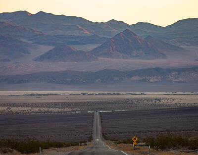 Photo of a landscape showing a long road with hills in the background. Death Valley National Park. Fall morning.